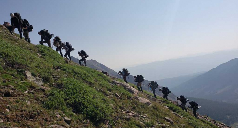 a group of gap year students hike up a grassy incline on an outward bound semester